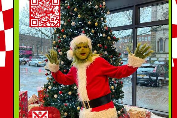 a character dresses up as the grinch beside a Christmas tree